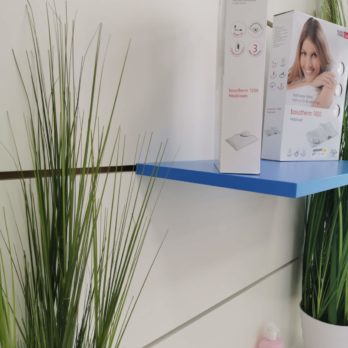 Verpackungen auf einem blauen Regal mit grünen Pflanzen im Hintergrund.