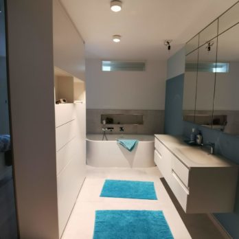 Helles Badezimmer mit Badewanne, Waschbecken und blauen Handtüchern auf dem Boden.