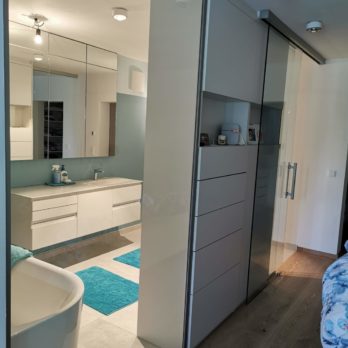 Ein modernes Badezimmer mit Glaswänden, einer Badewanne und einem Waschbecken mit Spiegeln.