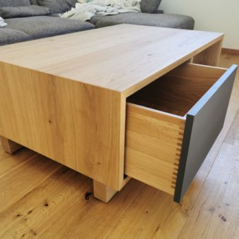 Ein moderner Couchtisch aus Holz mit einer offenen Schublade, auf einem Holzboden.