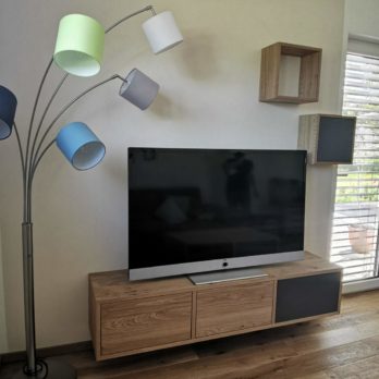 Schwarzer Fernseher auf einem Holzschrank mit einer modernen Stehlampe mit bunten Lampenschirmen.