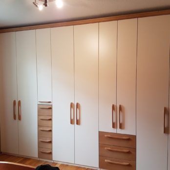 Ein moderner Kleiderschrank mit weißen Türen und Holzgriffen in einem Raum.