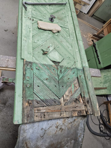 Restaurierungsprozess einer historischen Holztür – beschädigte Teile werden durch neues Holz ersetzt.