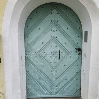 Alte Haustür mit Rundbogen, das Holz ist spröde und in die Jahre gekommen.