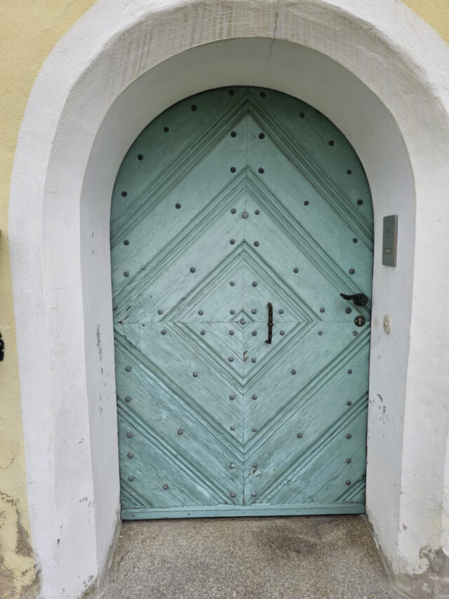 Alte Haustür mit Rundbogen, das Holz ist spröde und in die Jahre gekommen.
